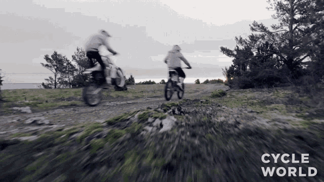 two people riding dirt bikes on a dirt road with the words cycle world visible