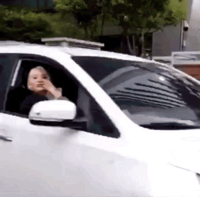 a woman is driving a white car and looking out the window .