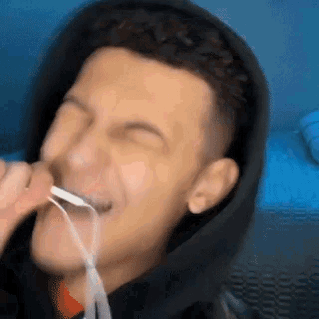 a man in a hoodie is holding a spoon in his mouth .