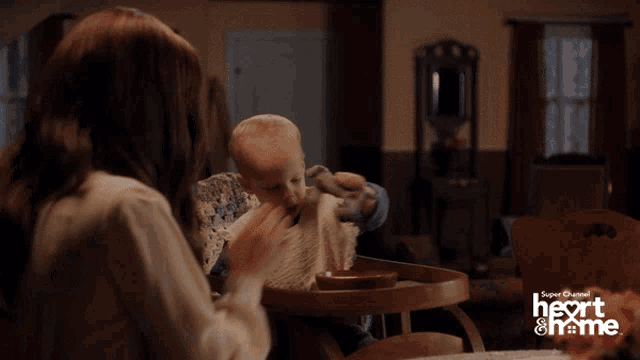 a baby in a high chair is being fed by a woman from the super channel heart and home