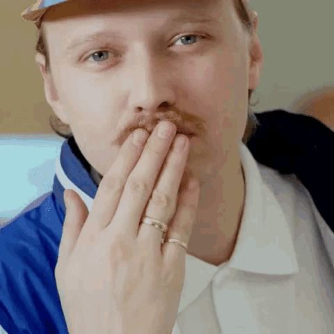 a man with a mustache and a ring on his finger covers his mouth