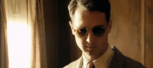 a man wearing sunglasses and a suit is looking at the camera