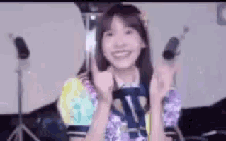 a young woman is giving a thumbs up sign while standing in front of a microphone .