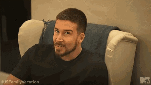a man with a beard is sitting on a couch with a blanket on it .