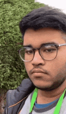 a young man with glasses and a beard is standing in front of a bush .