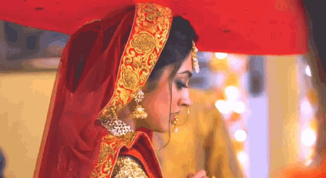 a bride in a red and gold dress is holding a red umbrella over her head .