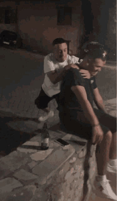 a man is sitting on another man 's shoulders with a bottle of water in front of him
