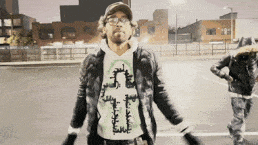 a man wearing a jacket and a hoodie with arabic writing on it stands in a parking lot