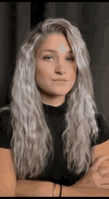 a woman with long blonde hair and a black shirt is looking at the camera .