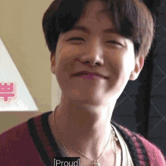 a young man wearing a red sweater and a necklace is smiling and looking at the camera .