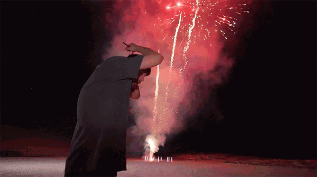 a man stands in front of a fireworks display with a cell phone in his hand