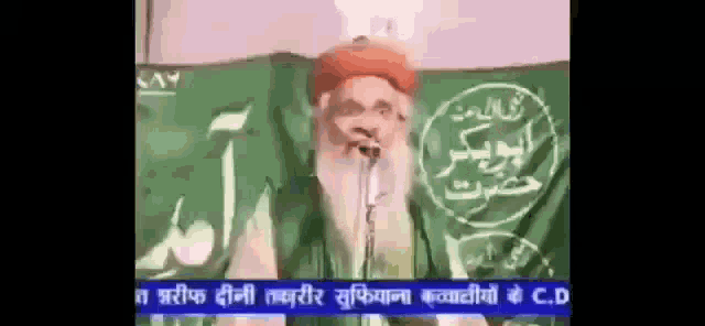 a man with a beard is speaking into a microphone while wearing a red turban
