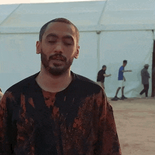 a man with a beard is standing in front of a tent in the desert .