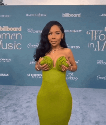 a woman in a green dress stands in front of a wall that says billboard