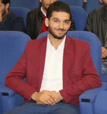 a man wearing a red jacket and a white shirt is sitting in a chair .