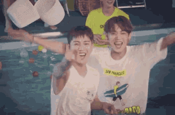 two young men are standing in a swimming pool with their arms outstretched and smiling .