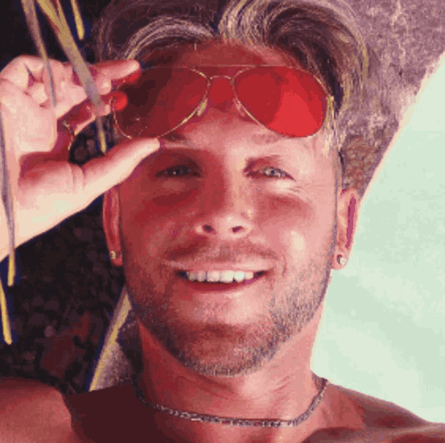 a man wearing red sunglasses and a choker smiles at the camera