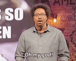 a man wearing glasses says oh my god in front of a brick wall