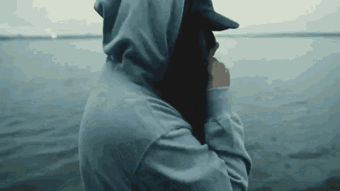 a woman wearing a hoodie and a hat is standing in front of a body of water .