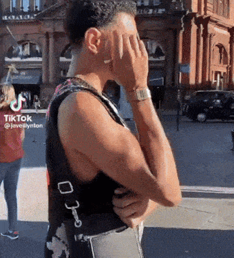 a man covering his face with his hand while wearing a watch and a floral tank top