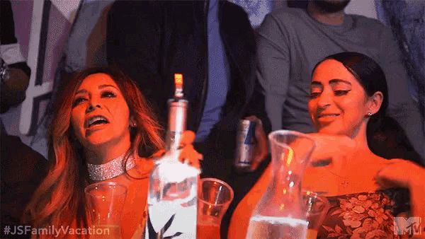two women are sitting at a table holding bottles of vodka and drinks .