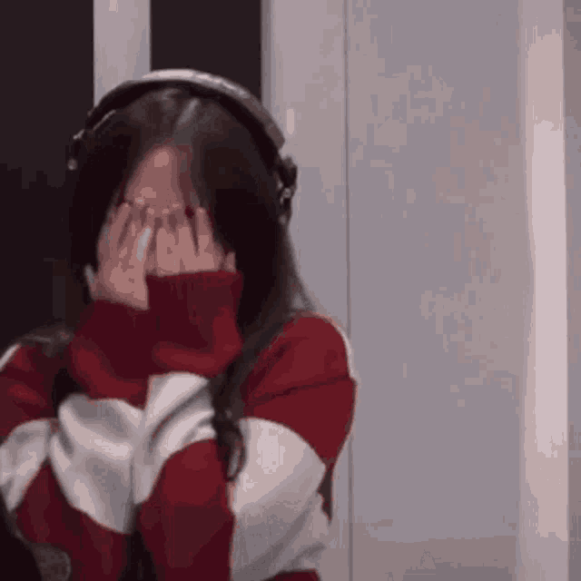 a woman wearing headphones and a red and white sweater covering her face