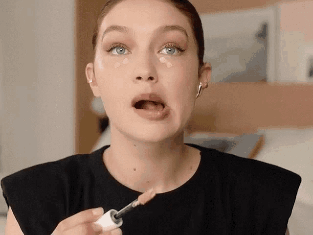 a woman is applying concealer to her face and making a funny face