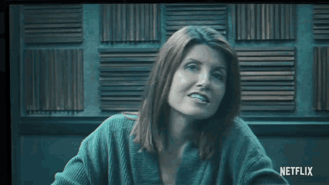 a woman in a green sweater is smiling in front of a netflix logo