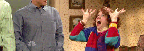 a woman in a colorful sweater is screaming with her hands in the air while a man stands behind her