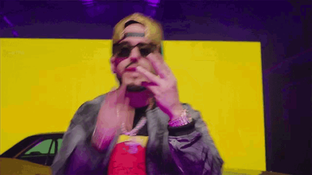 a man wearing sunglasses and a hat stands in front of a yellow background