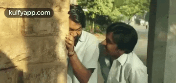 two men are standing next to each other behind a wall .
