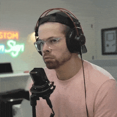 a man wearing headphones and glasses stands in front of a neon sign that says stom