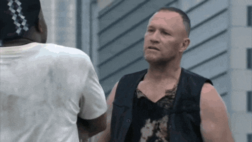 a man in a black vest is talking to another man in a white shirt .