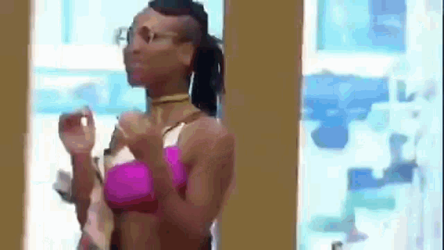 a woman in a pink bikini and glasses is standing in front of a window in a room .
