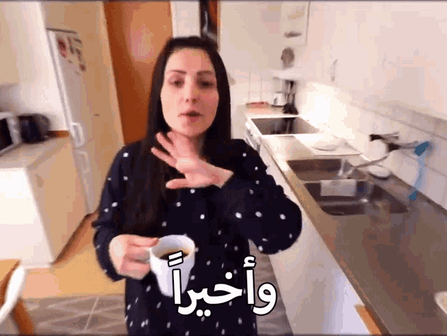 a woman holds a cup of coffee in a kitchen with arabic writing on the counter