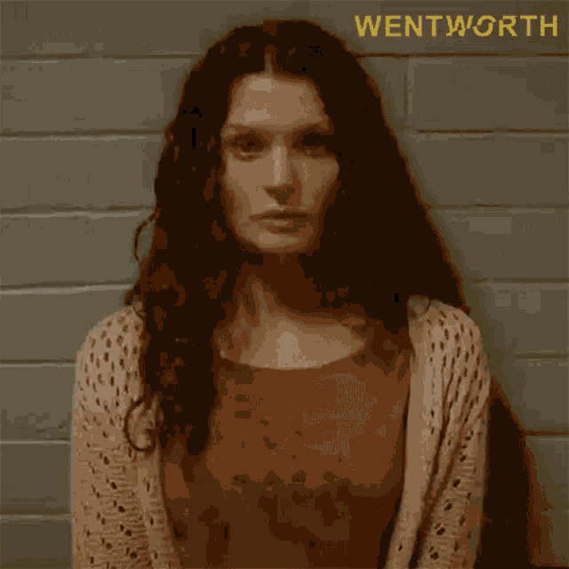 a woman with curly hair is standing in front of a brick wall with the word wentworth on it