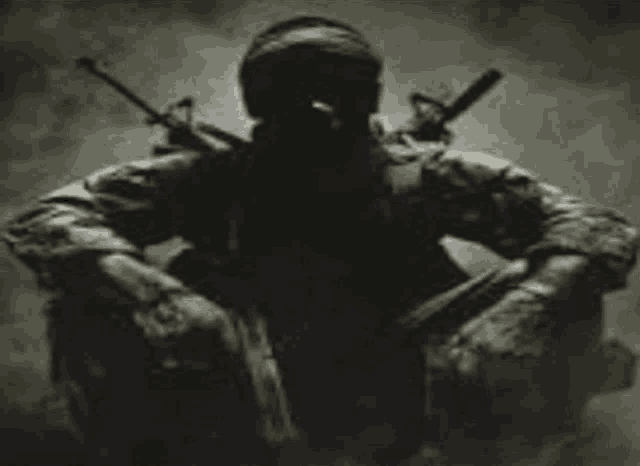 a soldier in a gas mask is kneeling down with two guns on his back .