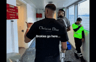 a man wearing a christian dior t-shirt stands in an airport