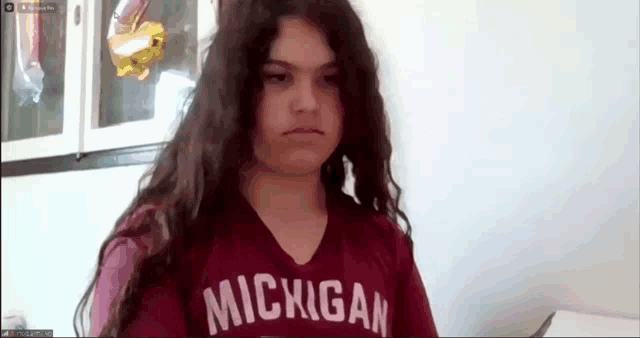 a girl wearing a michigan shirt is looking at the camera