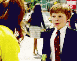 a young boy in a suit and tie talks to a woman in a yellow shirt