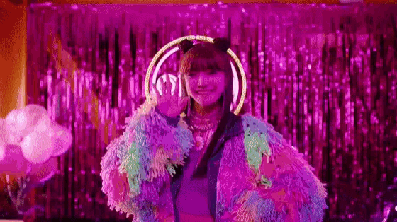 a woman in a colorful fur coat is standing in front of a pink curtain .