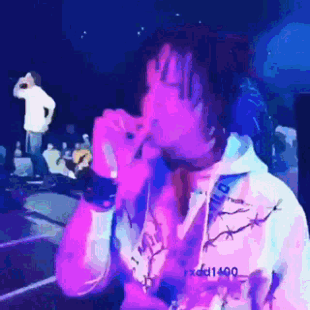 a man is singing into a microphone while wearing a white hoodie with barbed wire on it