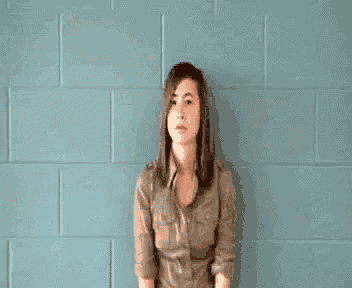 a woman is standing in front of a blue brick wall looking at the camera .