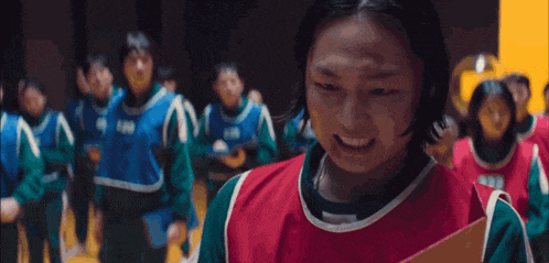 a woman in a red and green vest is standing in front of a group of people in a gym .