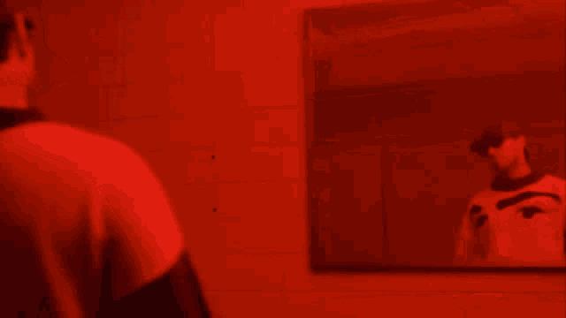 a man is looking at his reflection in a mirror in a red room