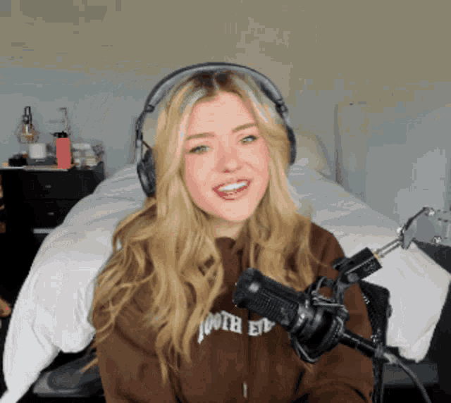 a woman wearing headphones and a brown hoodie with the word tooth on it stands in front of a microphone
