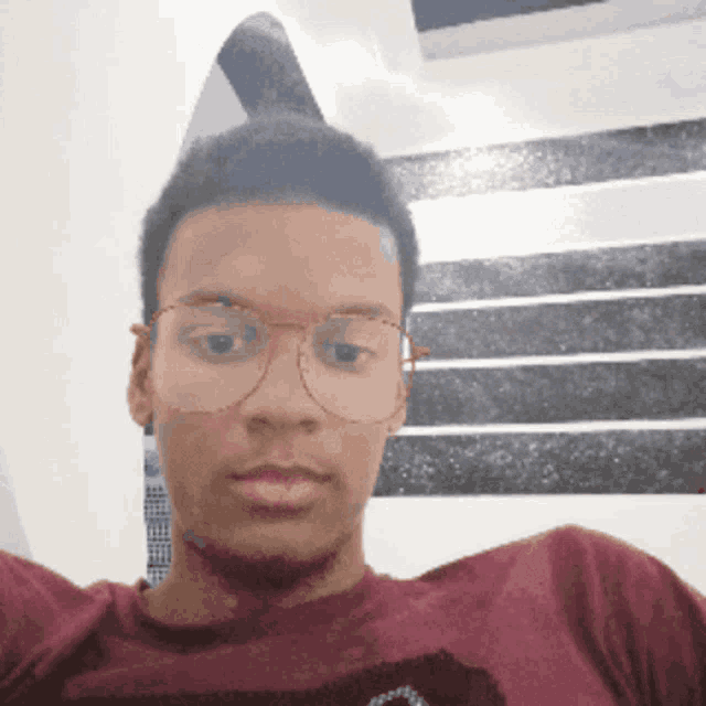 a young man wearing glasses and a maroon shirt looks at the camera