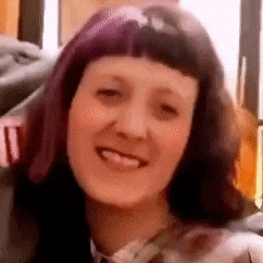 a close up of a woman 's face with purple hair smiling .