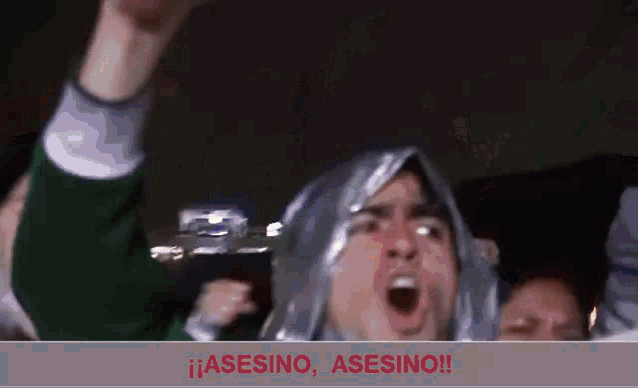 a man with a plastic bag on his head is screaming in front of a sign that says asesino asesino !!