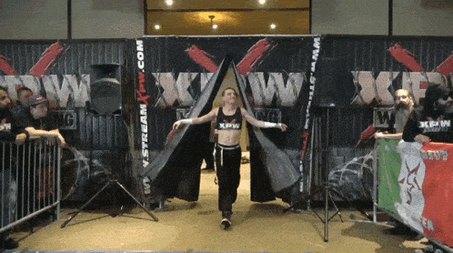 a woman in a xpaw outfit walks through a wrestling ring